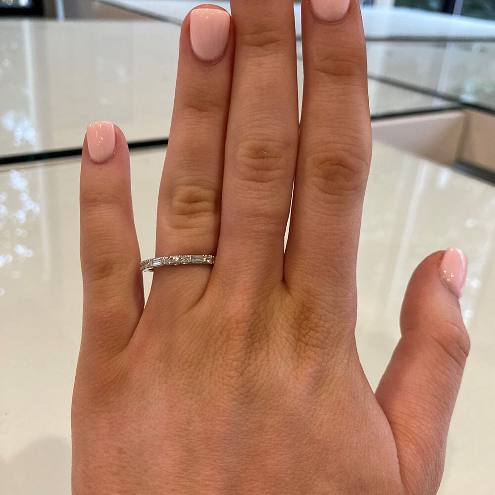 A close-up of a woman wearing a thin platinum band ring with round and baguette diamonds 