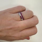 Hand wearing a ring with ruby and diamond stones on a plain background