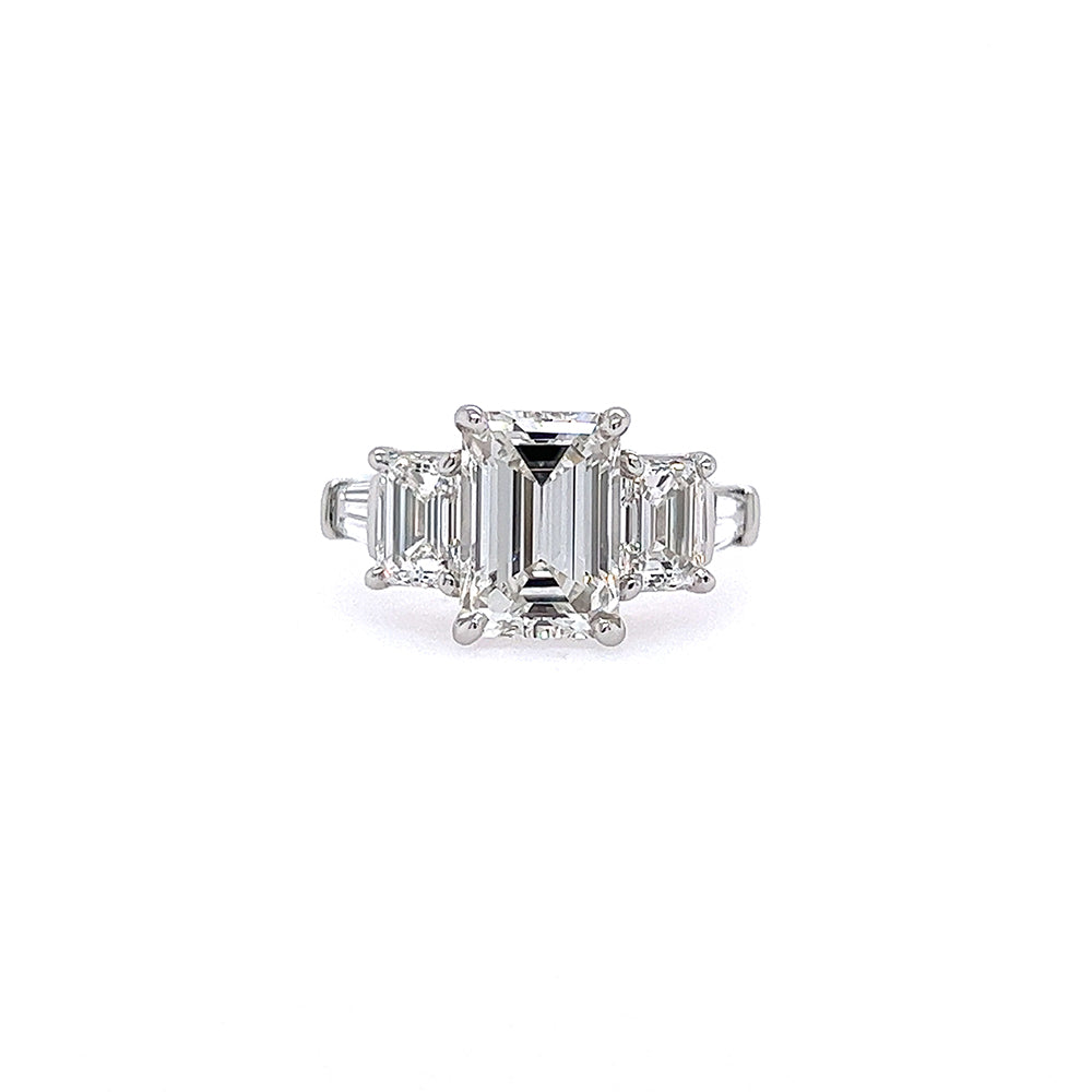 This image features an exquisite Platinum and Emerald Cut Diamond Three Stone Ring. The ring showcases a stunning emerald-cut diamond centered between two elegantly cut side stones, all encased in a sleek, polished platinum band.