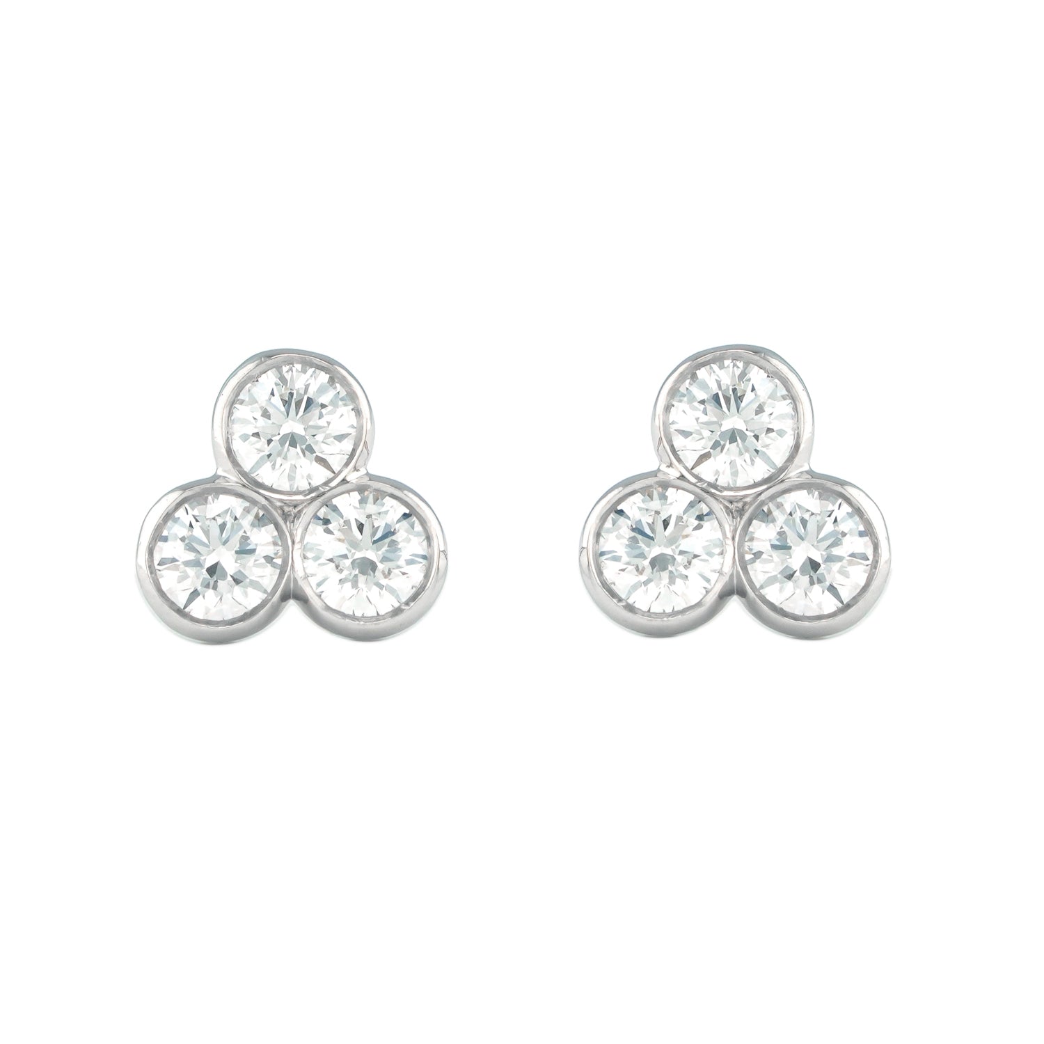 Pair of platinum earrings with three round diamonds on a white background