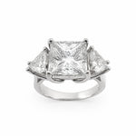 A three-stone diamond ring featuring a central princess-cut diamond flanked by two smaller trillion-cut diamonds in a platinum setting, shown on a plain white background.