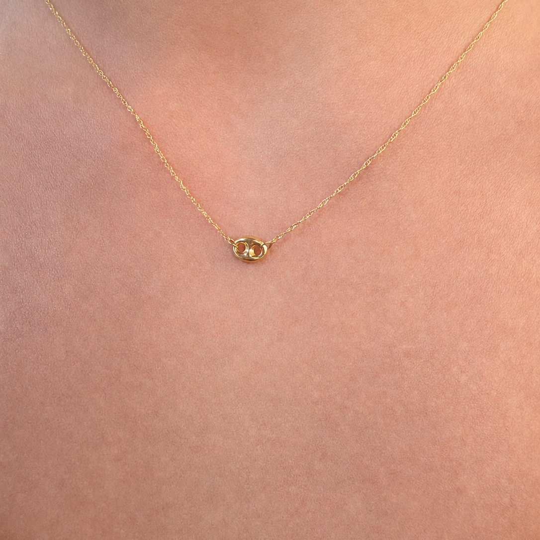 A delicate gold chain necklace with a small, polished gold oval pendant, shown worn on a person's neck against a light skin tone background.
