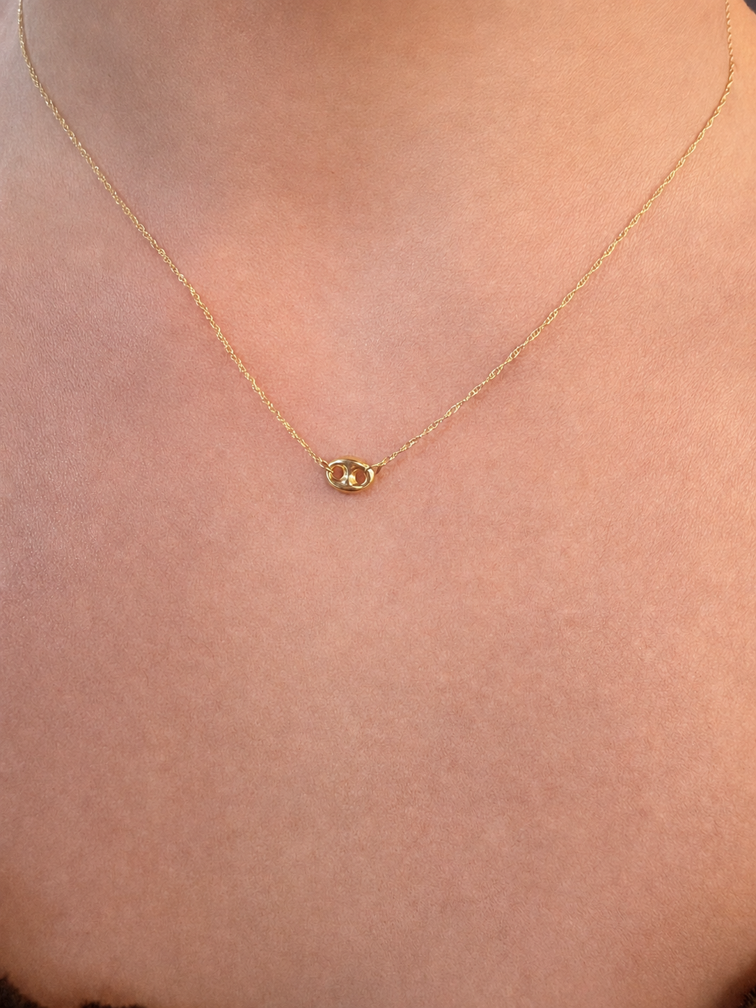 A delicate gold chain necklace with a small, polished gold oval pendant, shown worn on a person's neck against a light skin tone background.