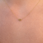 A delicate gold chain necklace with a small, polished gold oval pendant, shown worn on a person's neck against a light skin tone background.