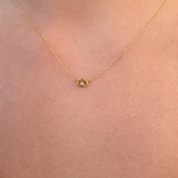 A delicate gold chain necklace with a small, polished gold oval pendant, shown worn on a person's neck against a light skin tone background.