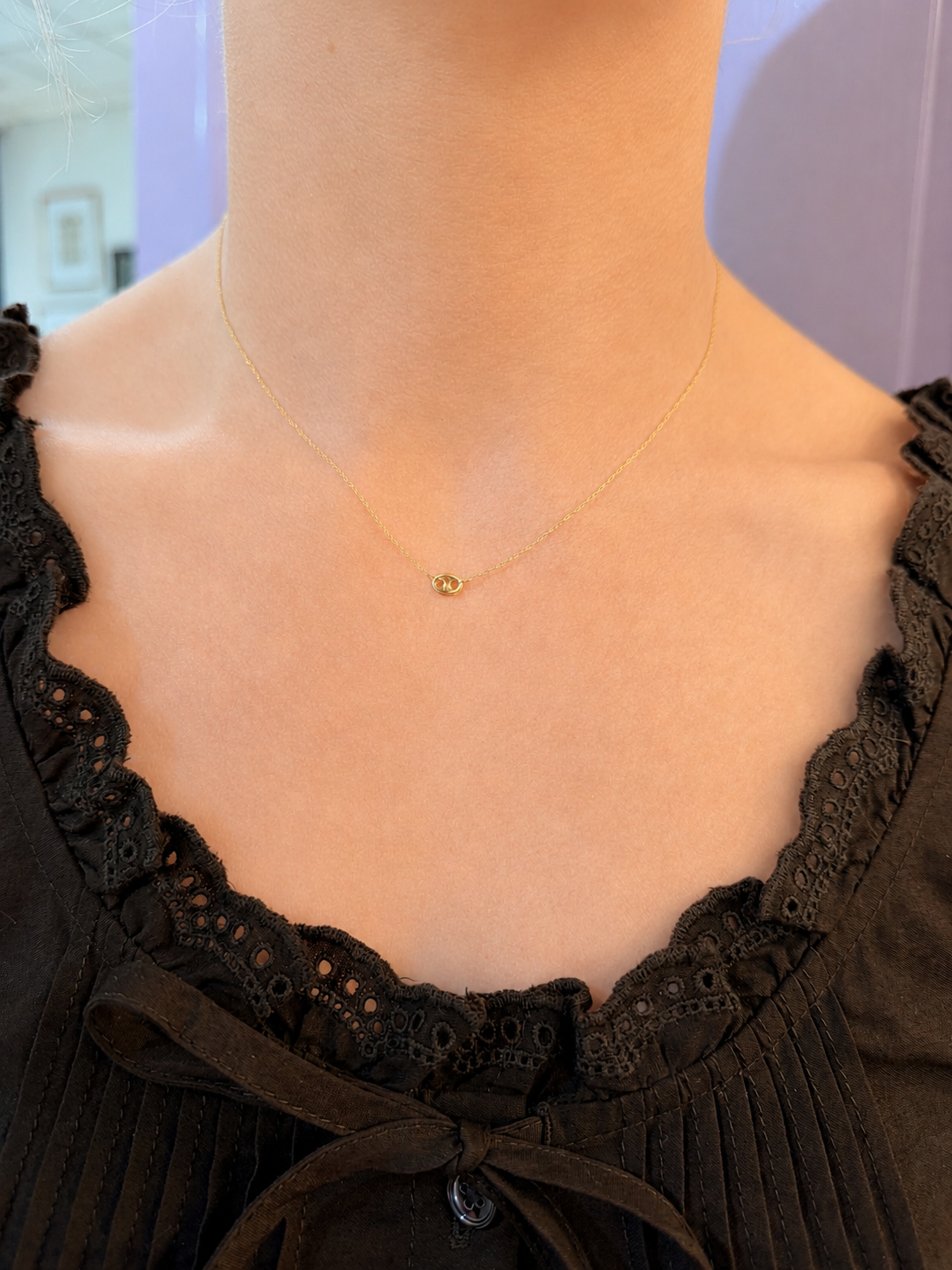 A delicate gold chain necklace with a small gold heart pendant, shown worn on a model's neck over a black lace-trimmed top.