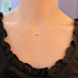 A delicate gold chain necklace with a small gold heart pendant, shown worn on a model's neck over a black lace-trimmed top.