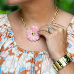 woman wearing an 18K gold necklace with a large rose quartz flower with a green peridot center 