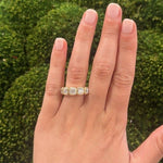 Hand wearing an 18K gold 2.5 carat diamond ring with a green blurred background