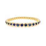 An 18K yellow gold stretch bracelet with blue bezel set sapphires.
