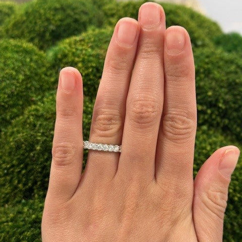Hand wearing a platinum shared prong set diamond ring 1.62 carats with a blurred green background