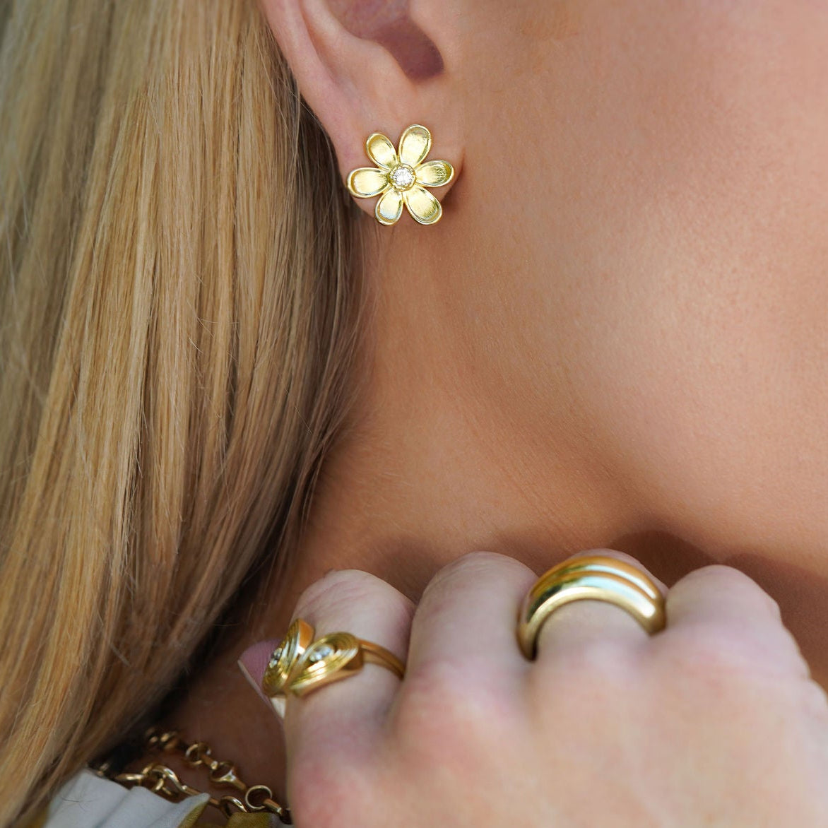 Close-up of a woman wearing 18K gold floral earrings and rings.