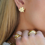 Close-up of a woman wearing 18K gold floral earrings and rings.