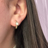 14K Gold earring with a small round bezel diamond worn by a woman with dark hair.