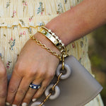 Hand holding a Loewe handbag with gold chain detail, wearing a gold Teardrop bracelet and ring.