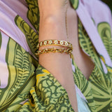 18K Gold bracelets designed by Temple St Clair on a woman's wrist with a green and white patterned garment