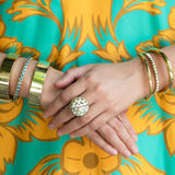 Close-up of woman's hands with gold bracelets and an estate Pearl ring against a floral-patterned fabric background.