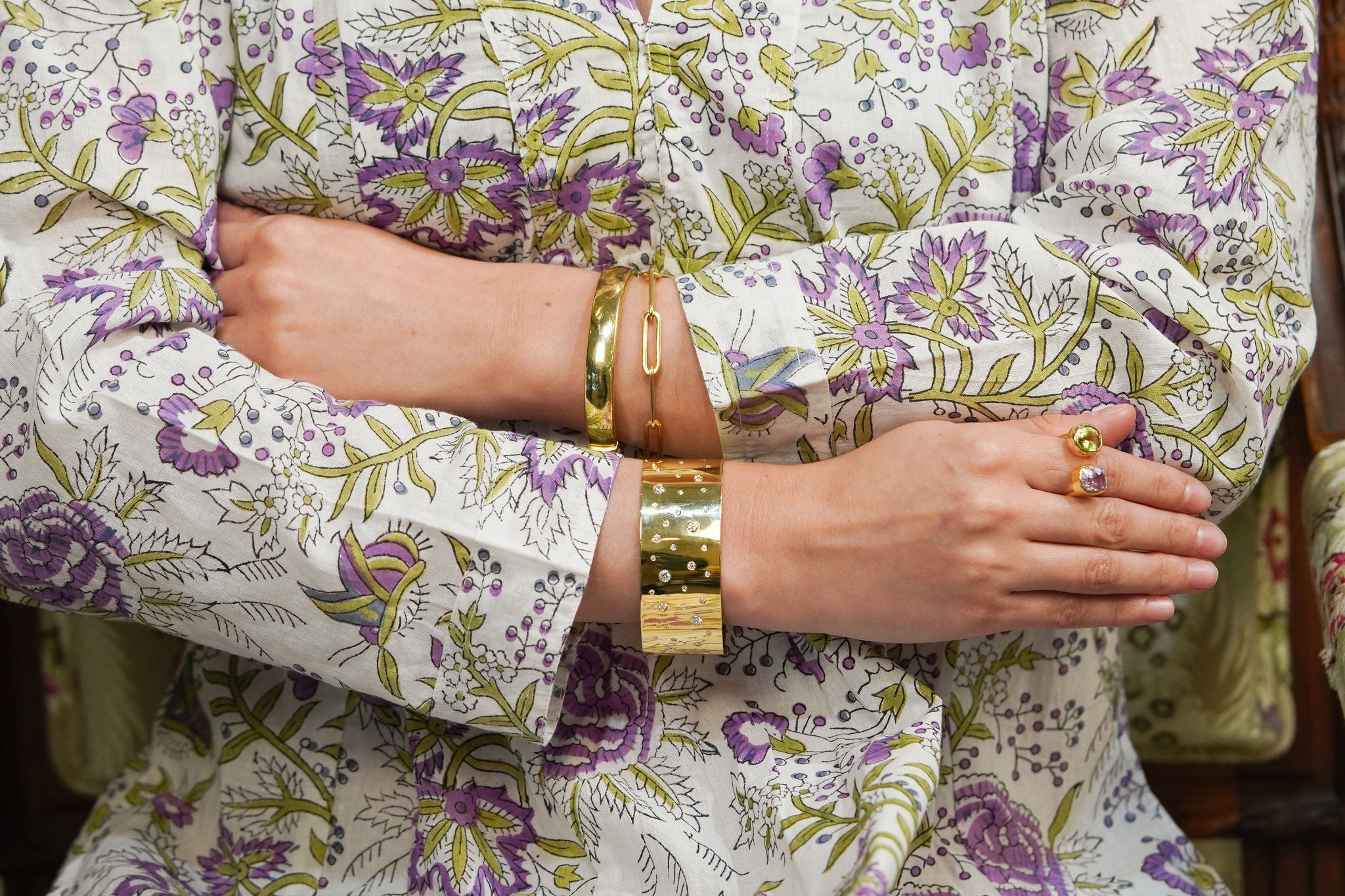 Woman wearing a floral outfit with 18K gold bracelets and rings.