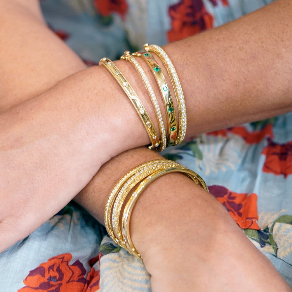 18K Gold bracelets on a woman's wrist with a floral-patterned fabric background