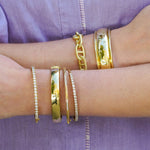 18K Gold bracelets on a woman's wrists against a purple fabric background