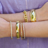 18K Gold bracelets on a woman's wrists against a purple fabric background