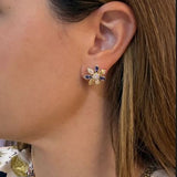 A close-up side profile of a woman wearing a 14K gold flower-shaped stud earring with sapphires and diamonds