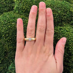 woman wearing an estate 18K Gold Cartier Donut ring with a diamond against a green hedge background