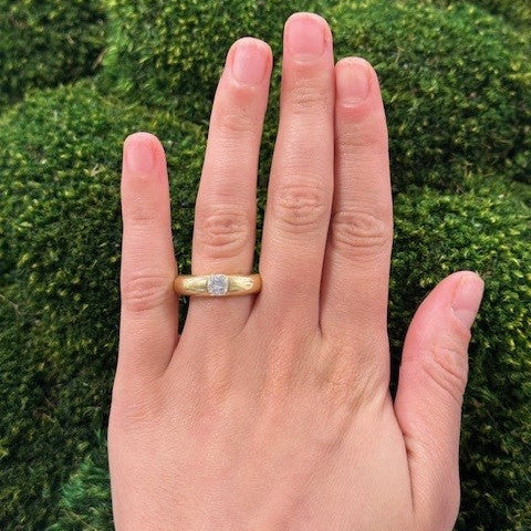 woman wearing an estate 18K Gold Cartier Donut ring with a diamond against a green hedge background