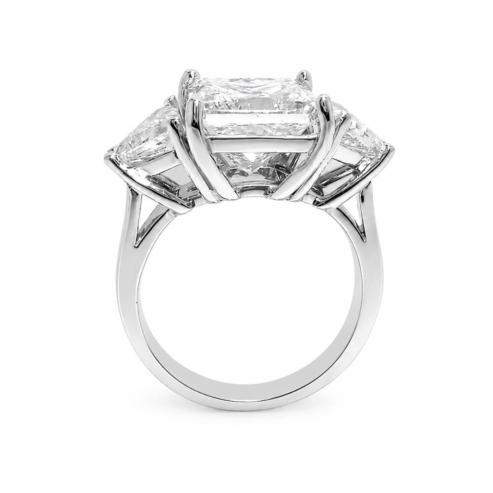 A three-stone diamond ring featuring a large rectangular center diamond and two smaller trillion-cut side diamonds in a polished platinum setting, shown against a plain white background.