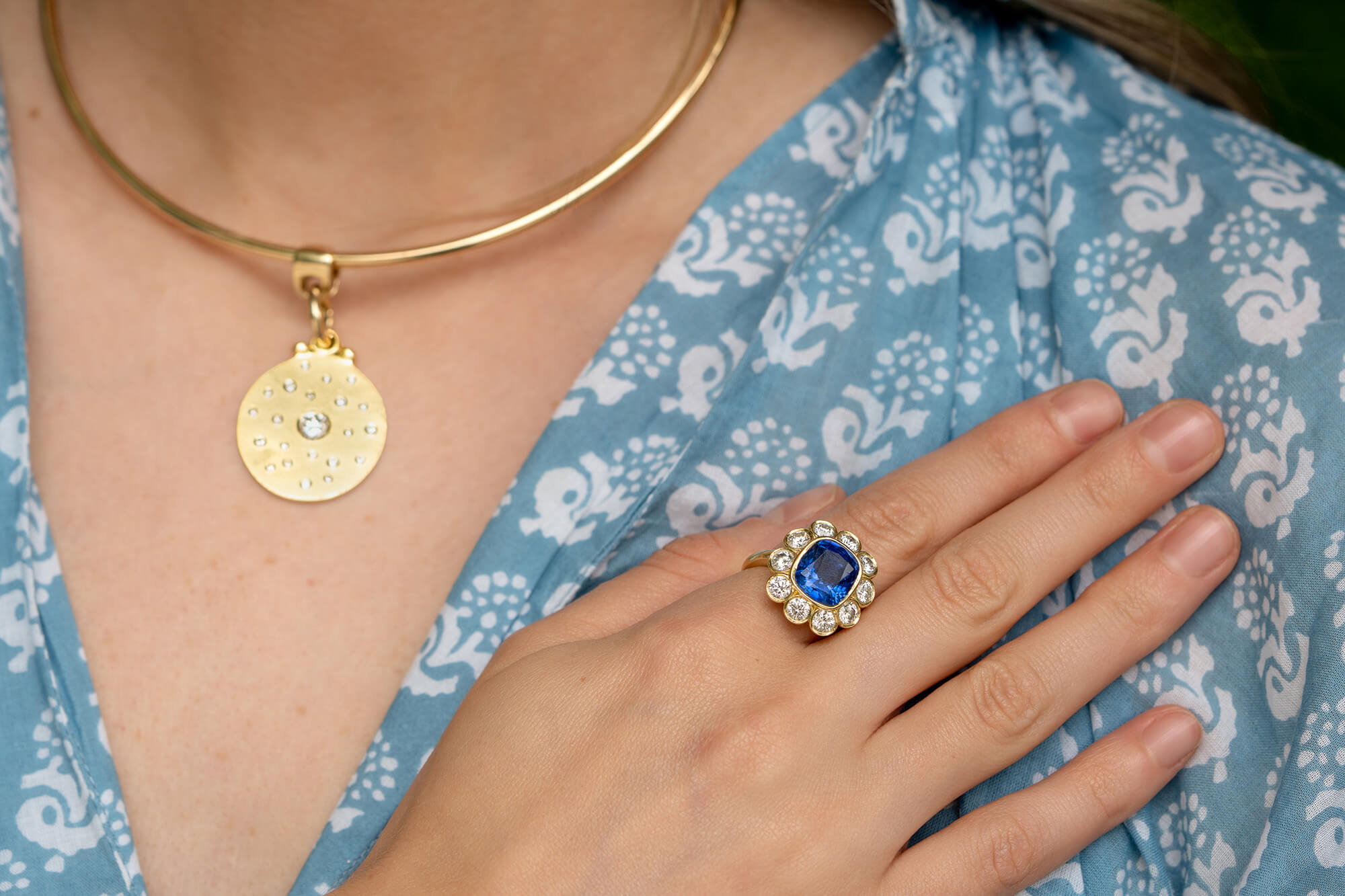 Woman wearing custom 18K yellow gold pendant necklace and custom sapphire and diamond ring 
