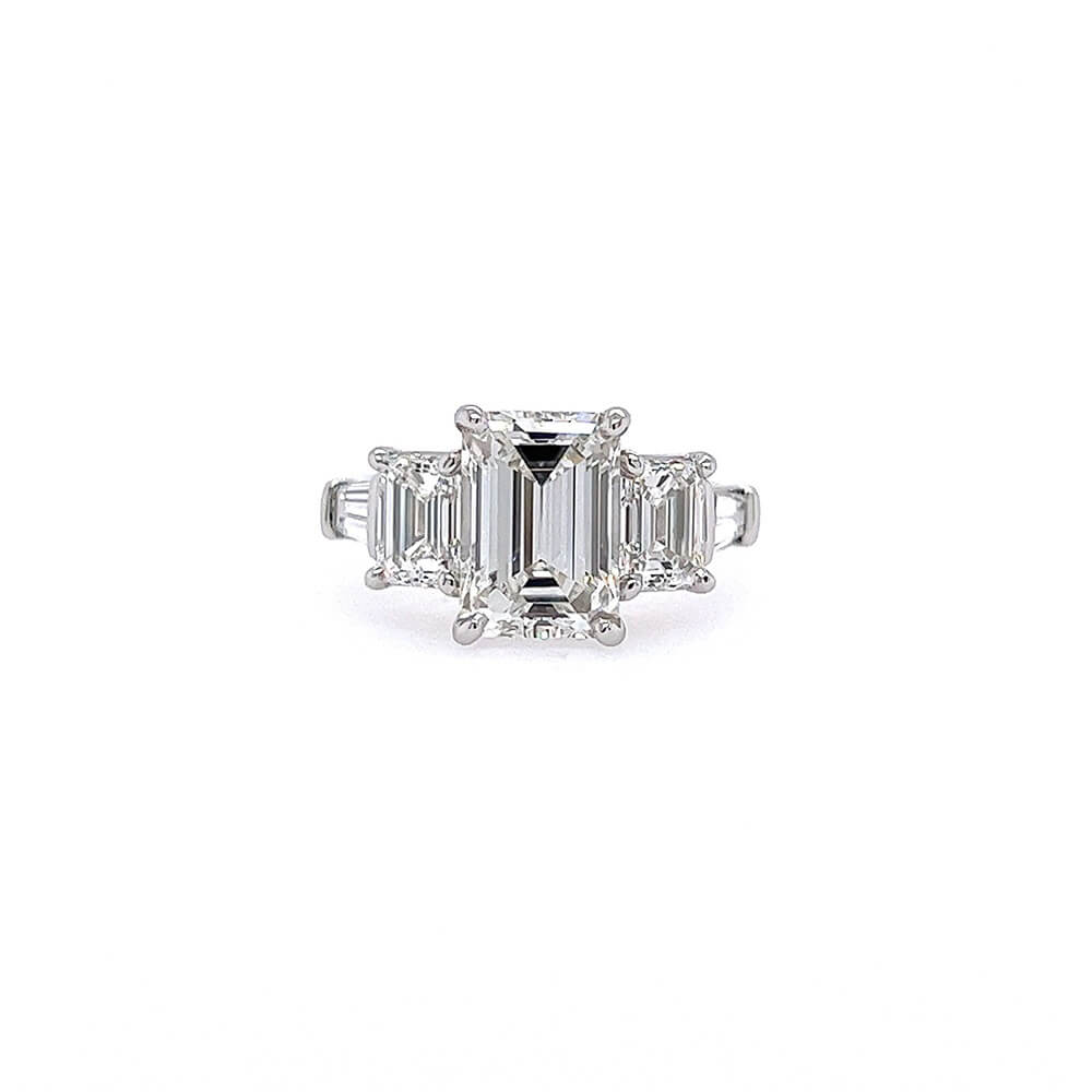 A platinum five-stone ring featuring a central emerald-cut diamond flanked by two emerald-cut diamonds, and tapered baguettes set in a polished silver band against a plain white background.