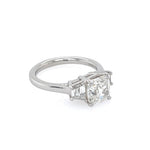A ring featuring a large cushion-cut diamond center stone with two smaller trapezoid diamonds on either side, set in a polished platinum band against a plain white background.