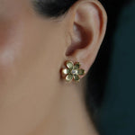 A close-up of a woman's ear wearing an 18K yellow gold flower-shaped stud earring with a clear center diamond. 