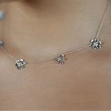 A close-up of a delicate 18K white gold chain necklace with three small flower-shaped charms, worn on a model's neck.