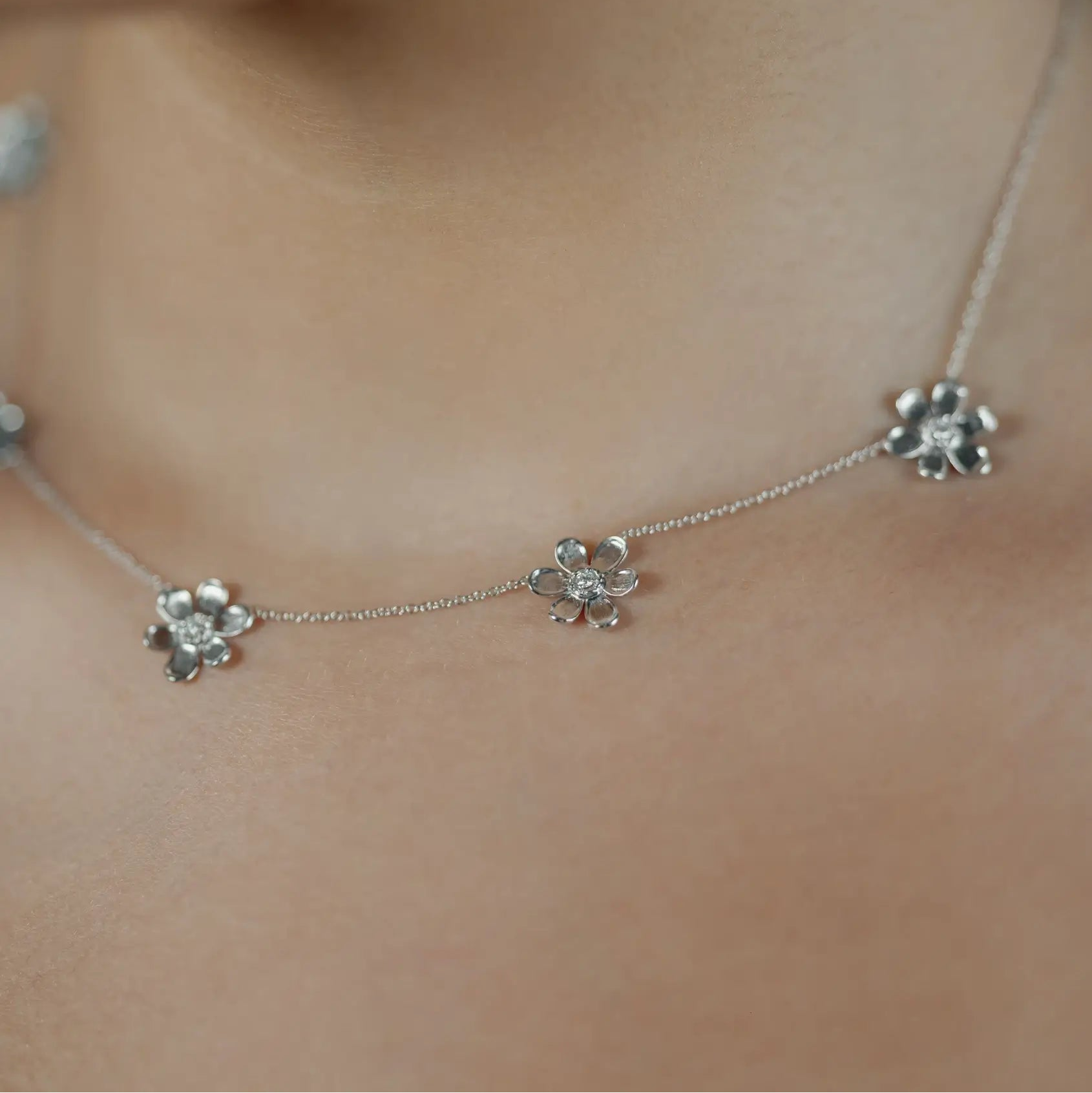 A close-up of a delicate 18K white gold chain necklace with three small flower-shaped charms, worn on a model's neck.