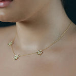 A close-up lifestyle shot of a model wearing a delicate 18K yellow gold chain necklace with three small flower charms with pave diamonds