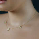 A close-up lifestyle shot of a model wearing a delicate 18K yellow gold chain necklace with three small flower charms with pave diamonds