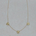 A delicate 18k yellow gold chain necklace featuring three small flower-shaped charms, each with clear diamonds, arranged on a light textured background.