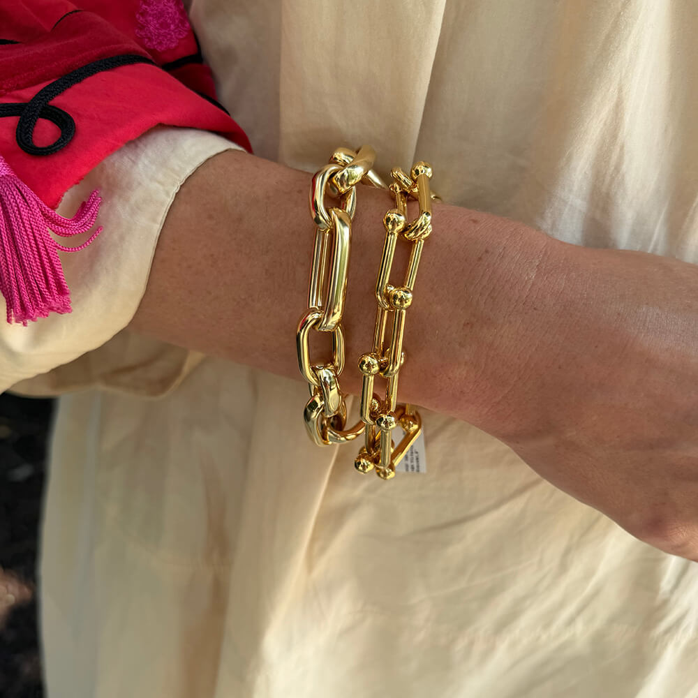 Two chunky 18K yellow gold chain link bracelets worn on a woman's wrist