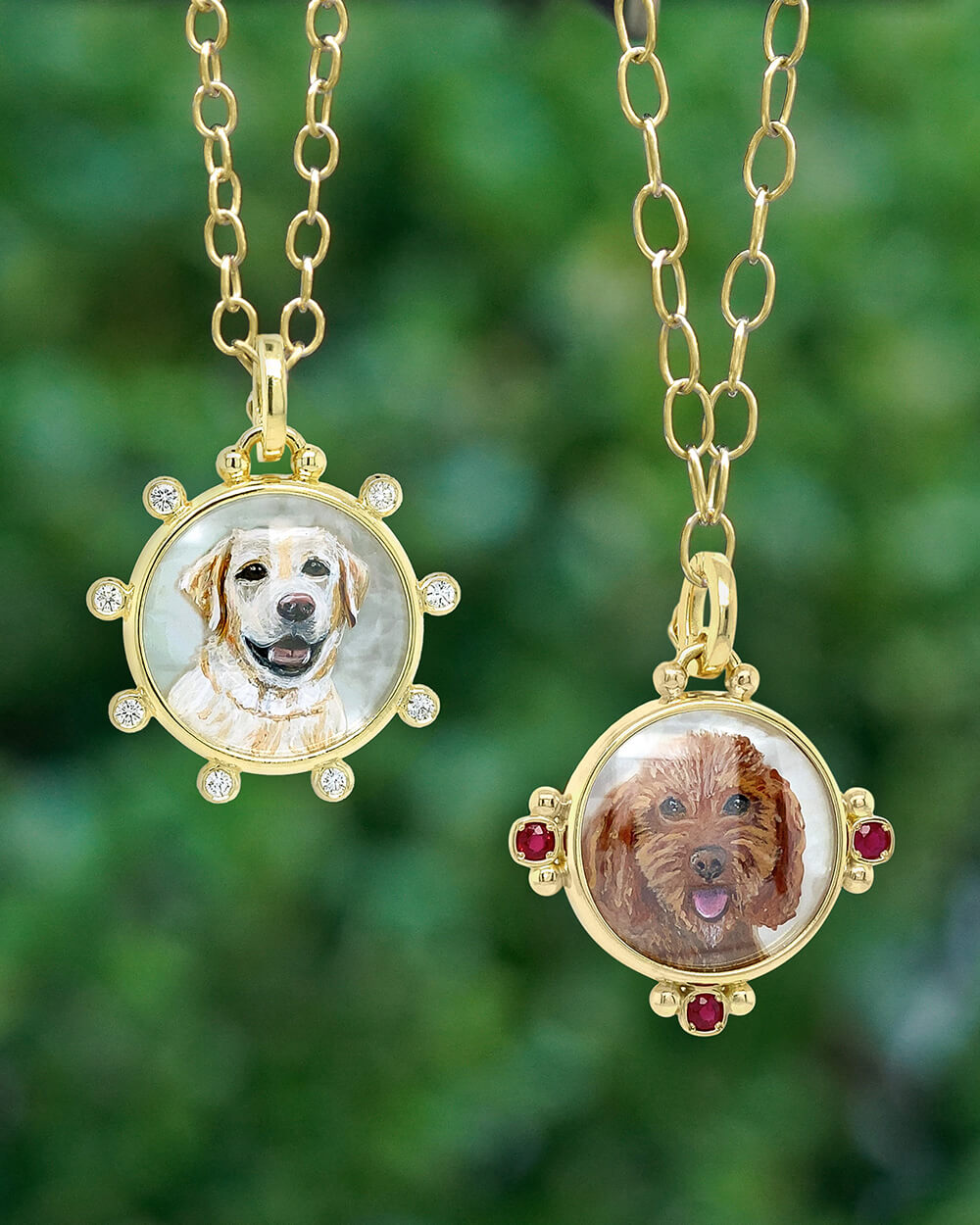 Two gold custom pet portrait necklaces hanging against a blurred green background. One pendant shows a light-colored dog with clear stones around the border, and the other shows a brown dog with red gemstone accents around the border.