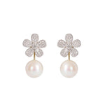 A pair of flower-shaped drop earrings featuring pavé-set clear diamonds and a single white pearl hanging below, shown on a plain white background.