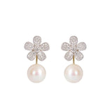 A pair of flower-shaped drop earrings featuring pavé-set clear diamonds and a single white pearl hanging below, shown on a plain white background.