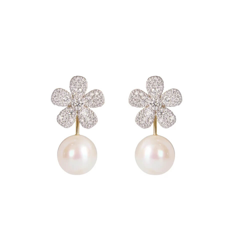 A pair of flower-shaped drop earrings featuring pavé-set clear diamonds and a single white pearl hanging below, shown on a plain white background.