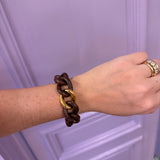 Hand wearing a brown and gold bracelet against a light purple background