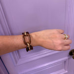 Hand wearing a brown chain bracelet and gold ring against a purple door.