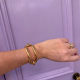 Hand wearing a gold bracelet and ring against a purple door