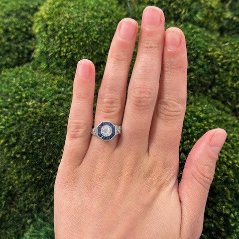 Hand wearing an estate ring with Sapphires and Diamonds against a green mossy background