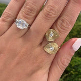 Hand wearing two gold rings with gemstones against a blurred green background