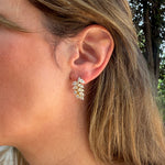 A close-up of a woman's ear wearing a 18K yellow gold leaf-shaped stud earring set with clear pear-shaped diamonds.