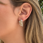 A close-up of a woman's ear wearing a 18K yellow gold leaf-shaped stud earring set with clear pear-shaped diamonds.